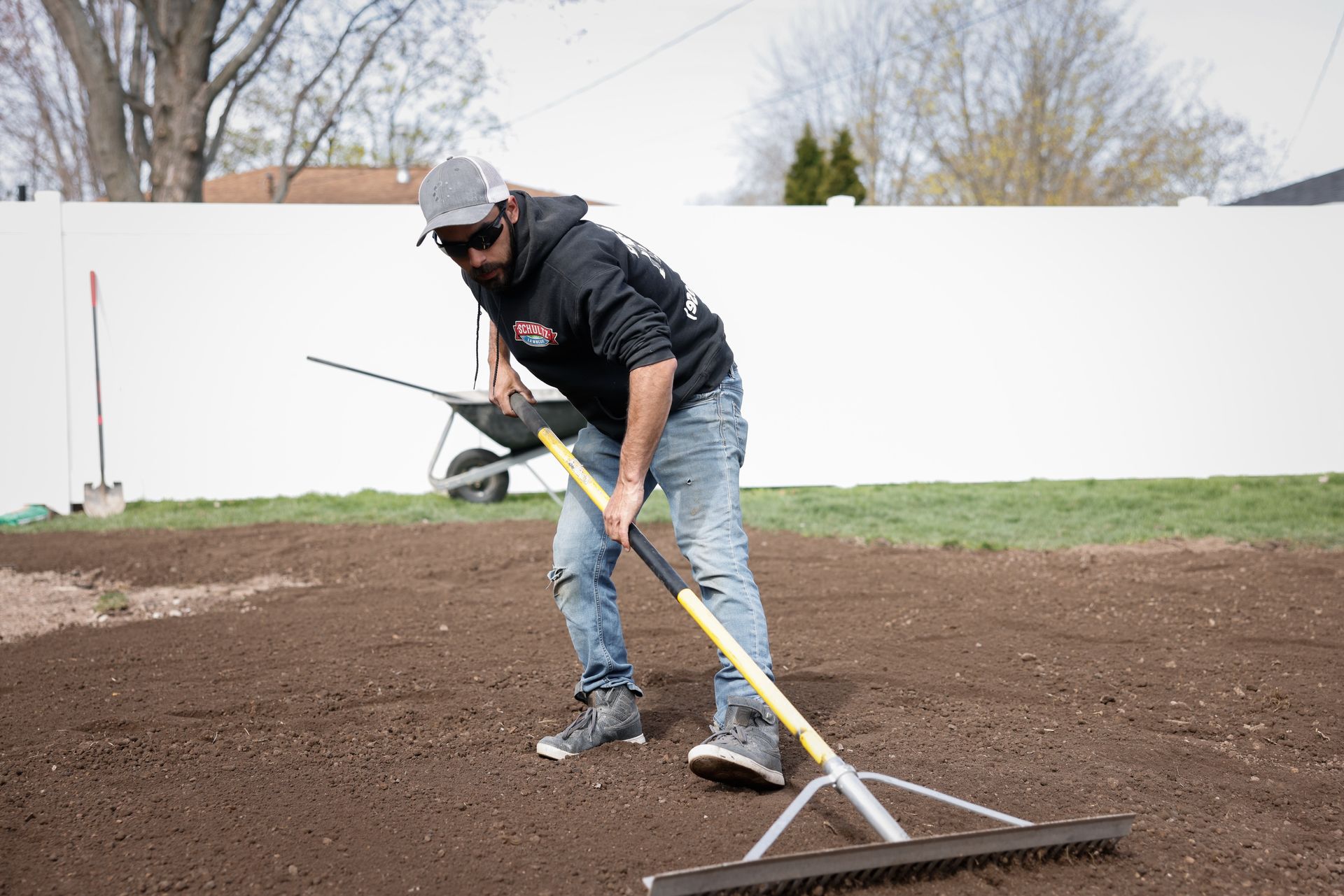 A man is raking dirt in a backyard with a rake.