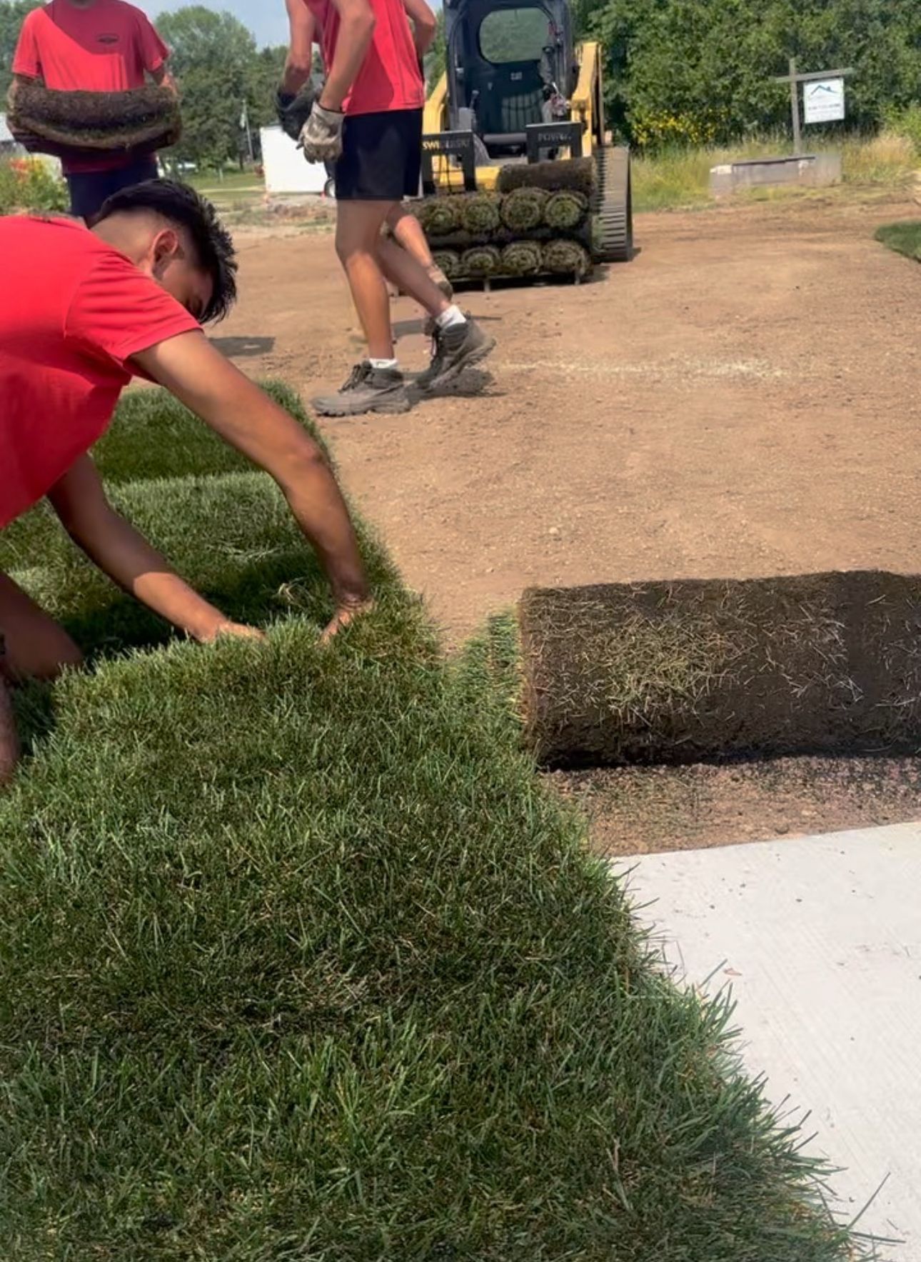 A man in a red shirt is kneeling down next to a pile of grass.