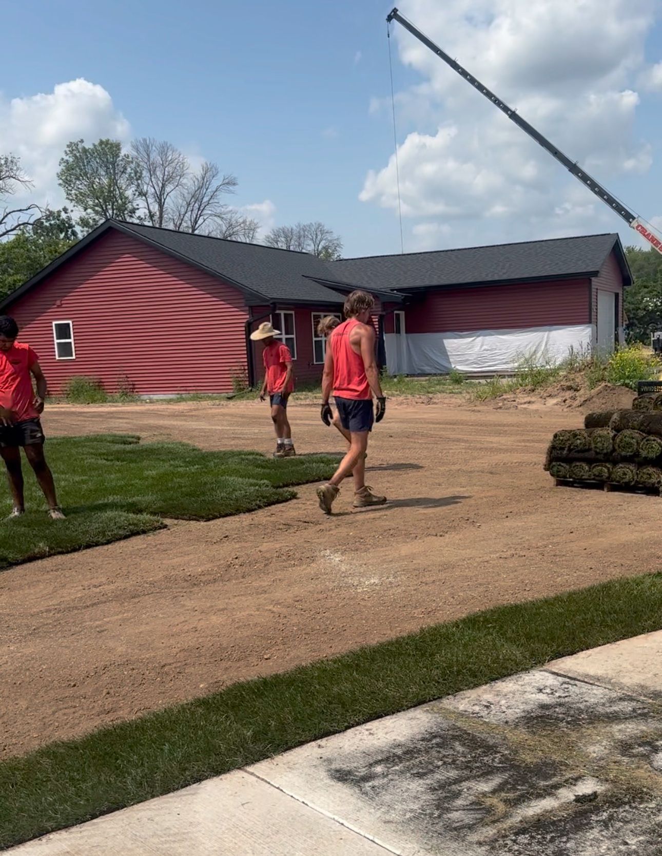 A group of people are walking down a dirt road in front of a red house.