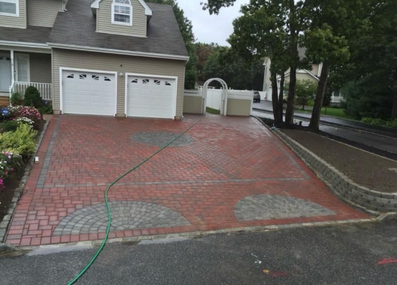 A newly paved asphalt driveway with stone curbing, blocked off by yellow caution tape between two suburban houses.