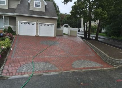 A newly paved asphalt driveway between two houses, bordered by cobblestones and blocked by yellow caution tape.
