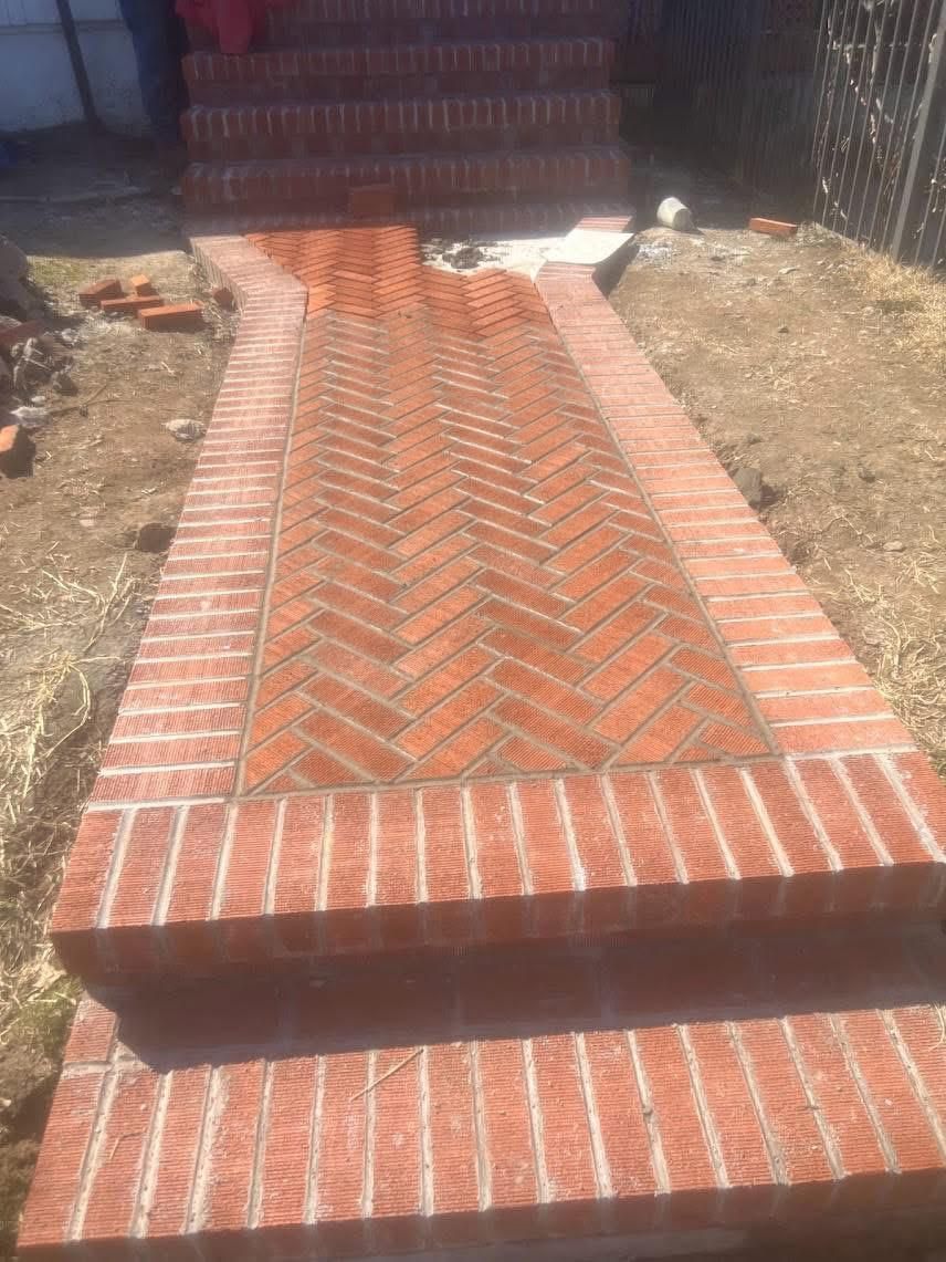 A brick walkway with a herringbone pattern leads to a set of brick stairs outdoors.