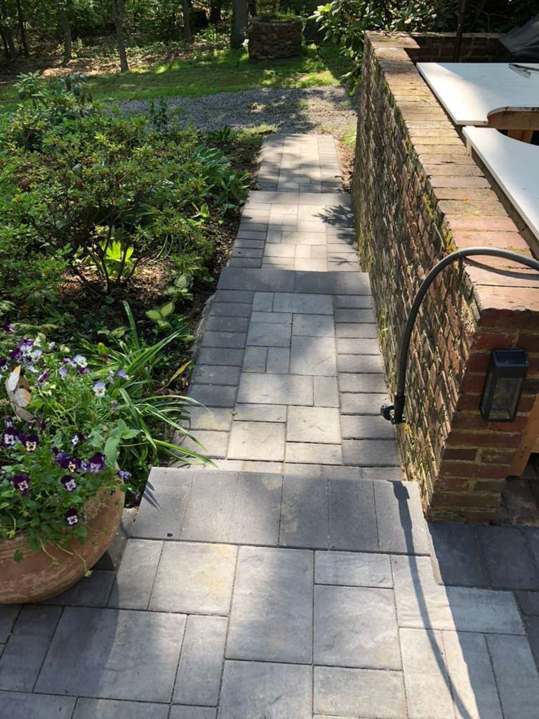 A paver walkway leads down steps next to a brick wall and a flower pot on a patio.