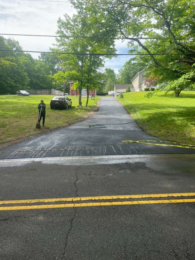 A person stands next to a freshly paved driveway entrance at the edge of a road with double yellow lines.