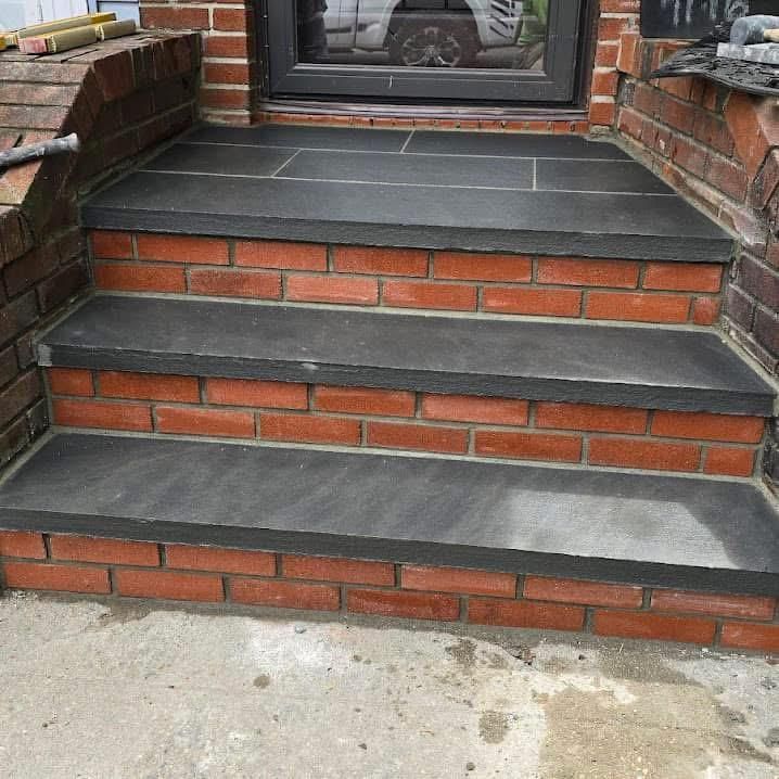 Three stone steps with dark grey treads and red brick risers lead up to a doorway.