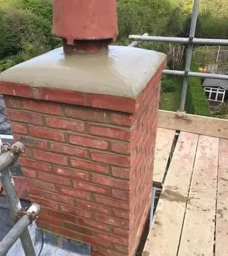 A red brick chimney topped with a fresh, smooth concrete crown and a terracotta chimney pot on a rooftop scaffold.