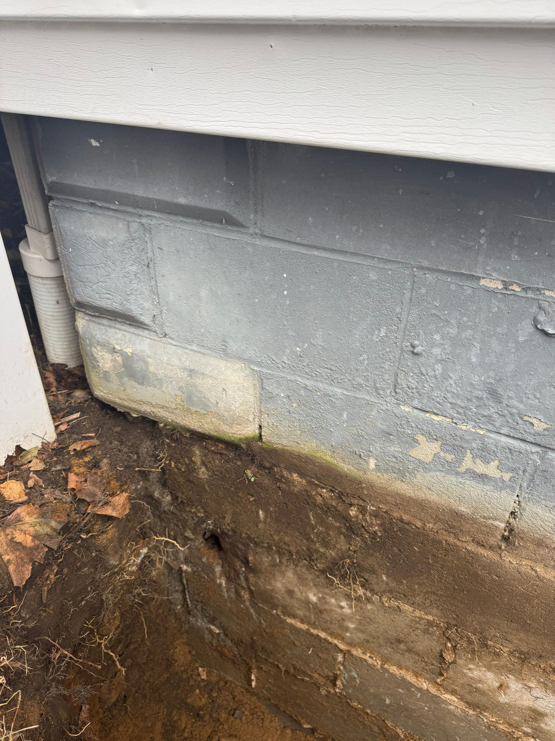 A close-up of a concrete block foundation wall showing visible soil line, discoloration, and a vertical pipe.