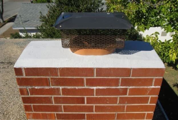 A brick chimney on a roof topped with a white concrete crown and a black metal spark arrestor cap.