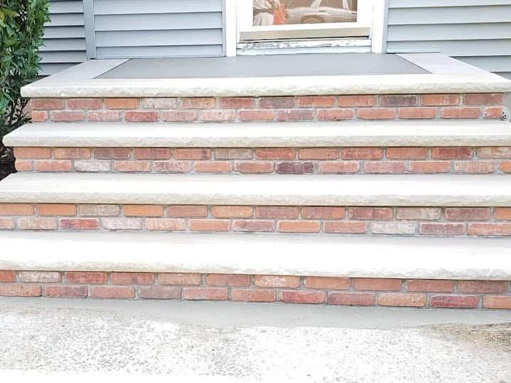 Four exterior steps featuring red brick risers and light-colored stone treads leading to a residential doorway.