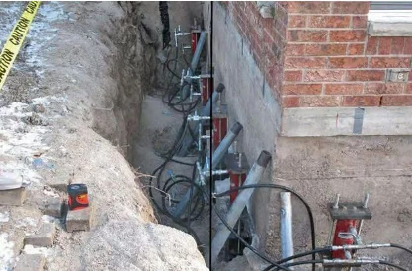 Hydraulic steel piers installed along a brick house foundation in an excavated trench for structural stabilization.