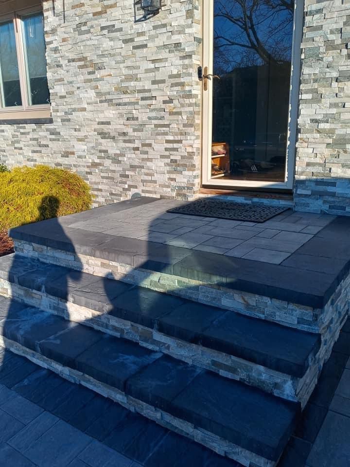 Three stone steps with dark slate treads leading to a house entrance with a stone-veneer exterior.