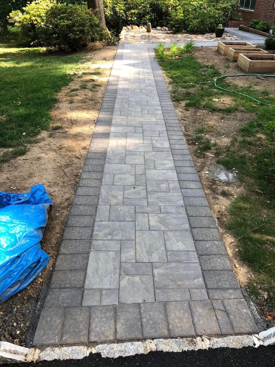 A straight outdoor stone walkway made of gray rectangular pavers with a dark gray border, leading toward a garden.