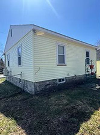 Side view of a yellow-sided house with white trim against a blue sky.