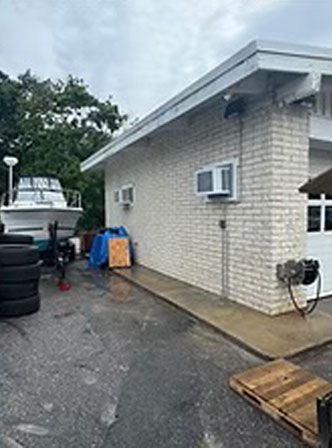 A boat on a trailer next to a brick building with air conditioners and a garage door, on an overcast day.