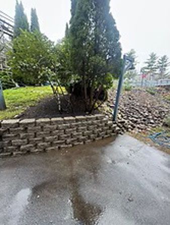 Retaining wall made of gray blocks near a tree and wet pavement.