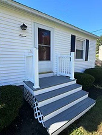 White house with gray steps leading to the front door. White railings and lattice detail. Blue sky.