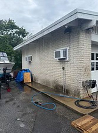 A building's brick exterior being pressure washed. A boat is on a trailer next to the building.