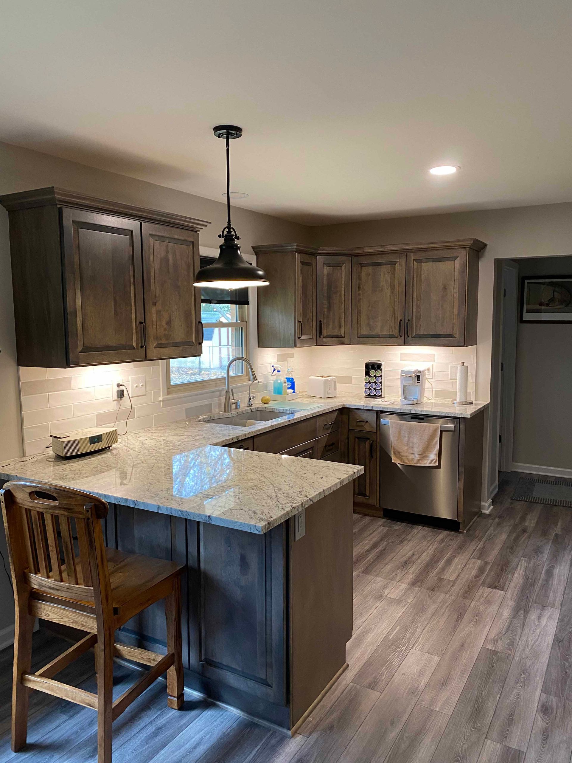A kitchen with wooden cabinets , granite counter tops , stainless steel appliances and a wooden chair.