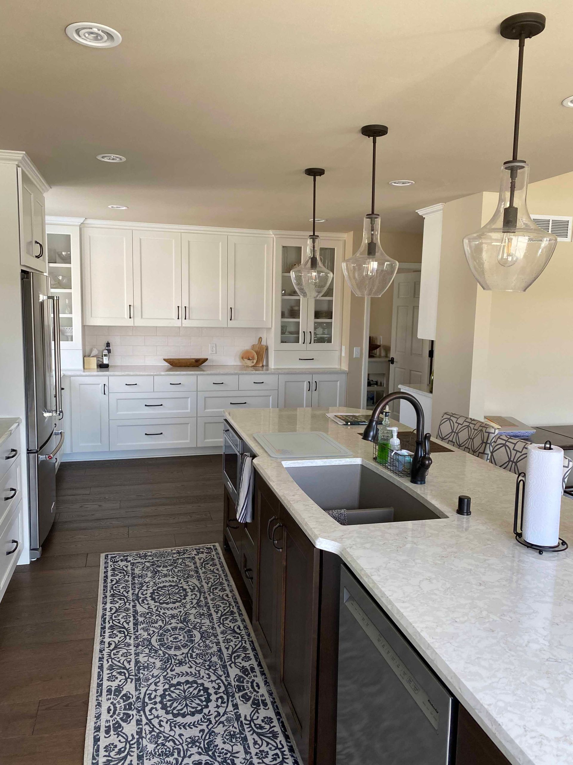 A kitchen with white cabinets , stainless steel appliances , a sink , and a rug.