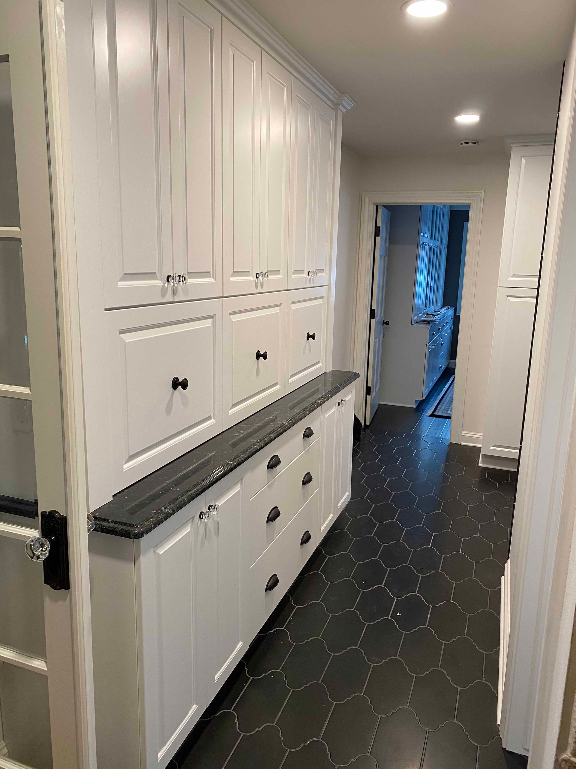 A hallway with white cabinets and black tile floors in a house.