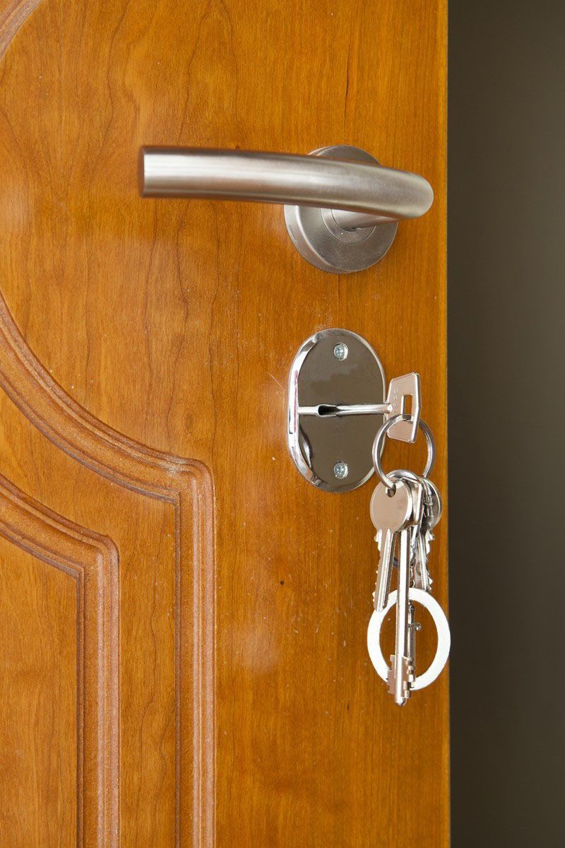Wooden door with silver handle and lock, keys hanging.