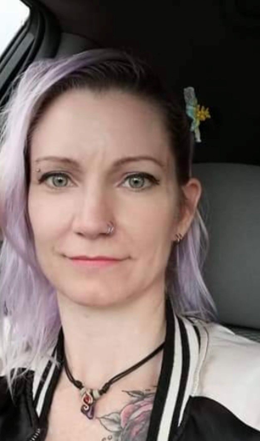 A woman with purple hair and a nose ring is sitting in a car.