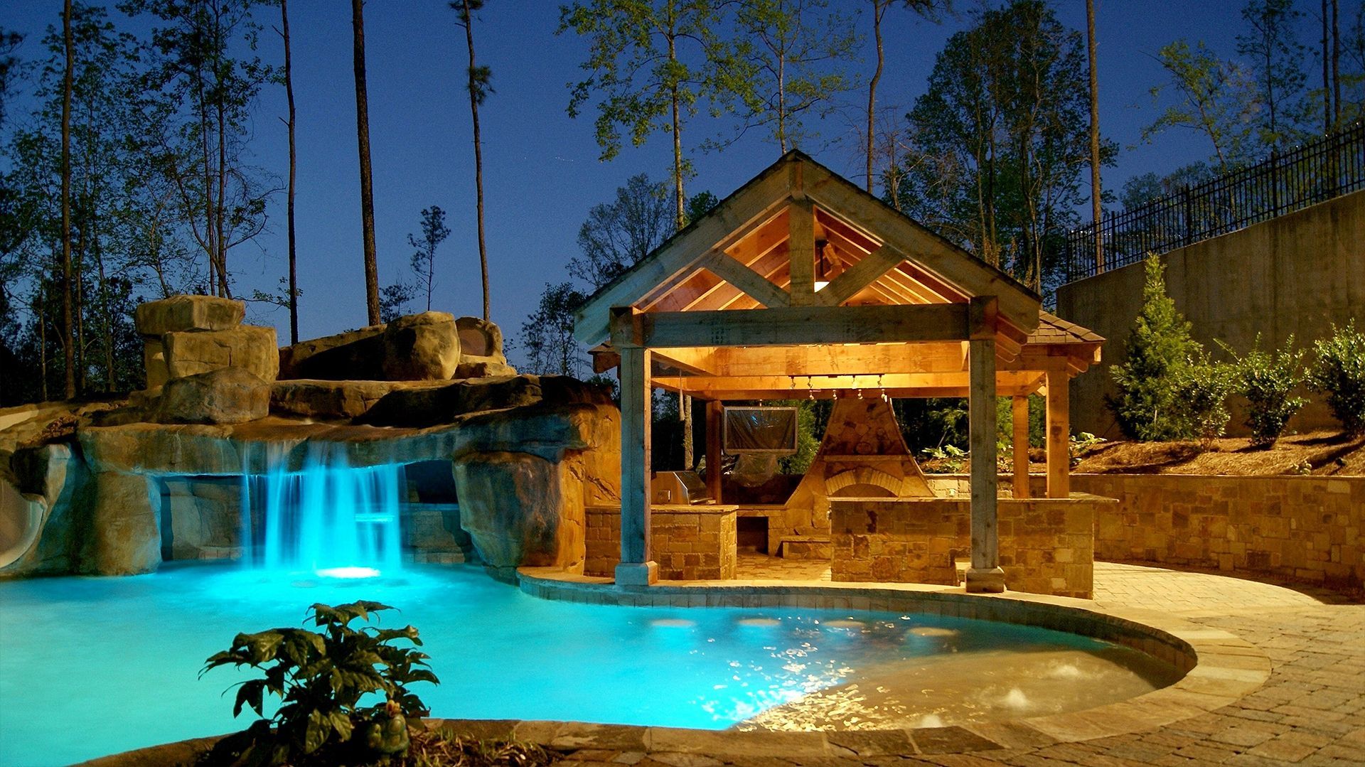 a large swimming pool with a waterfall and a gazebo at night
