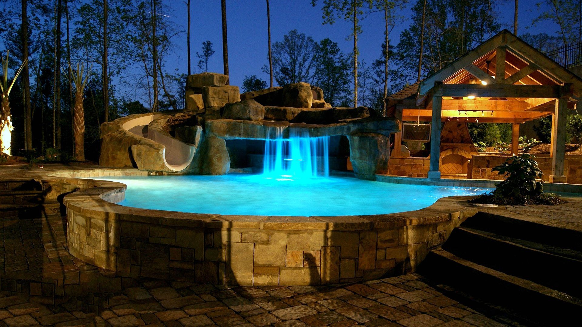 a large swimming pool with a waterfall in the middle is lit up at night