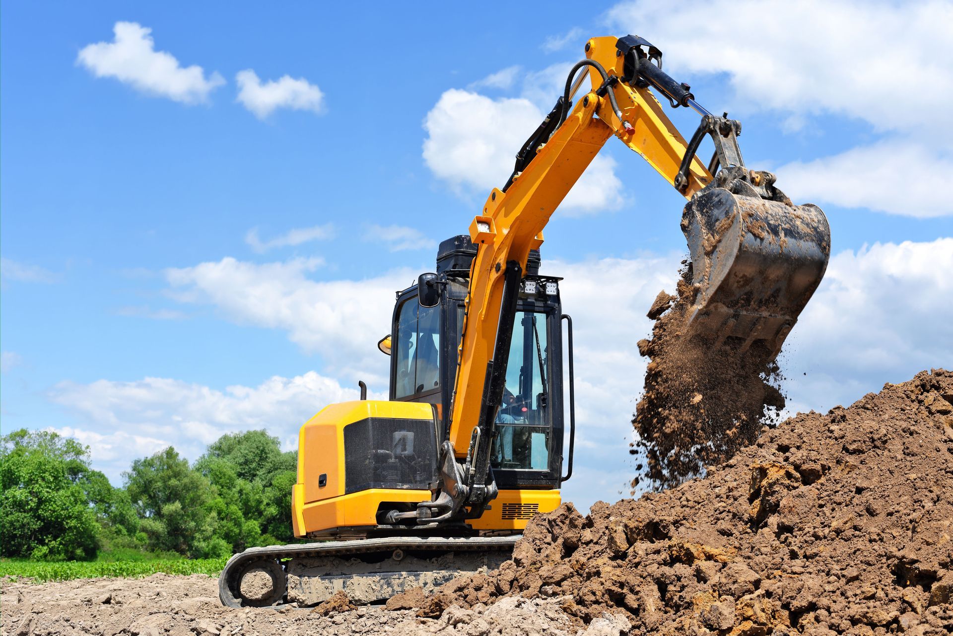 Yellow excavator digging dirt under a blue sky.