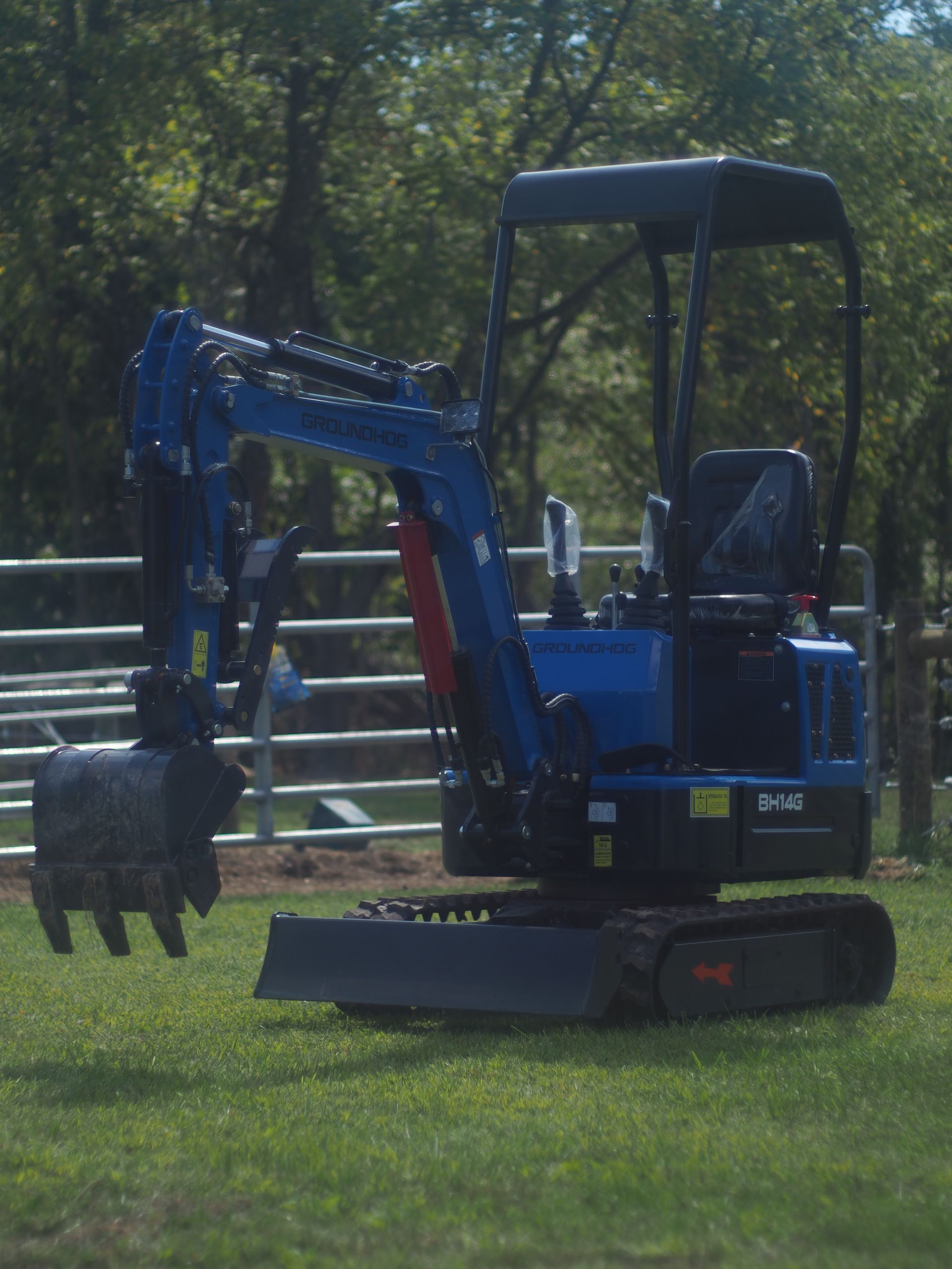 Blue mini excavator on green grass with trees in the background.