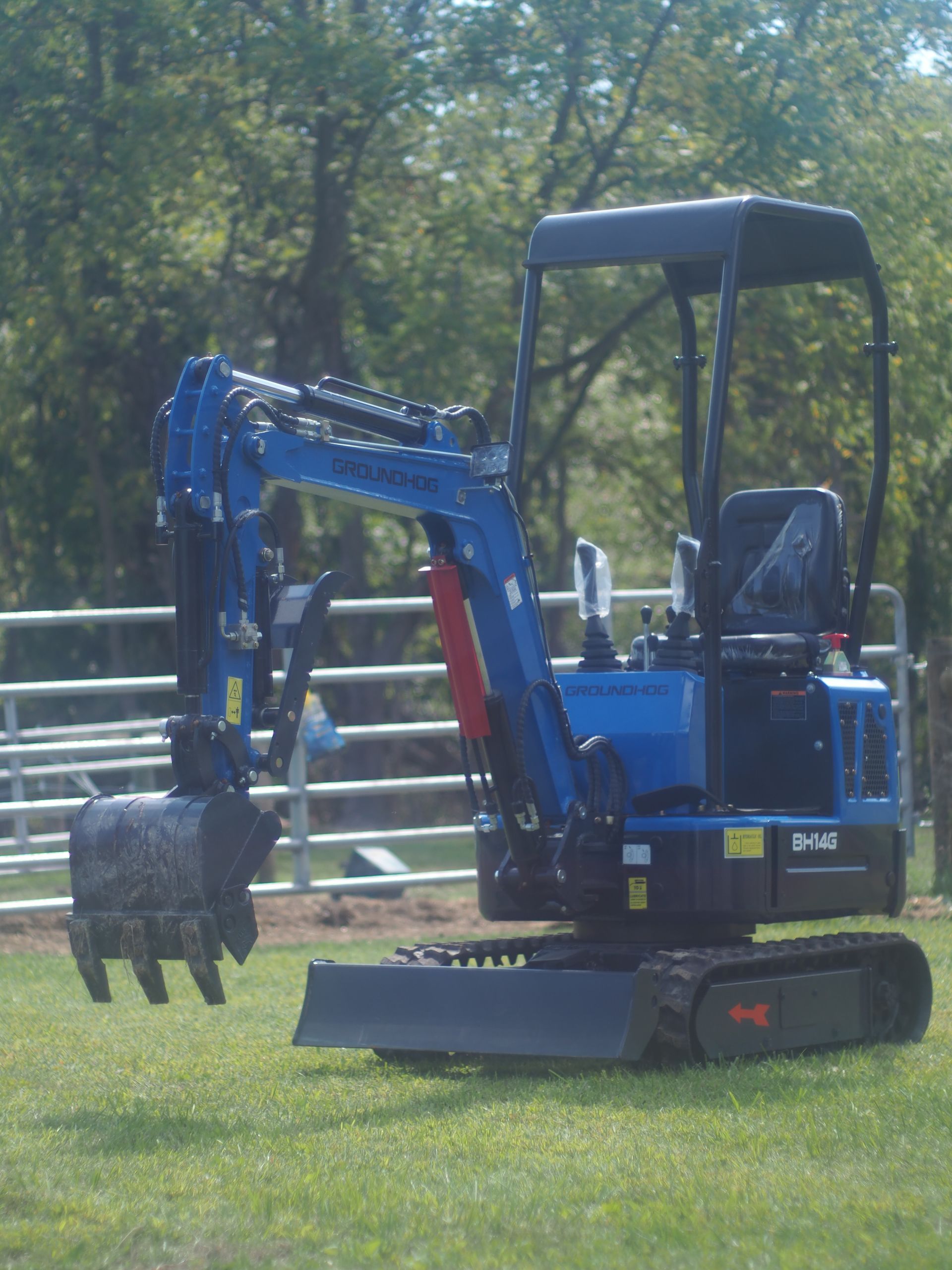 Blue mini excavator on grass, trees in background.