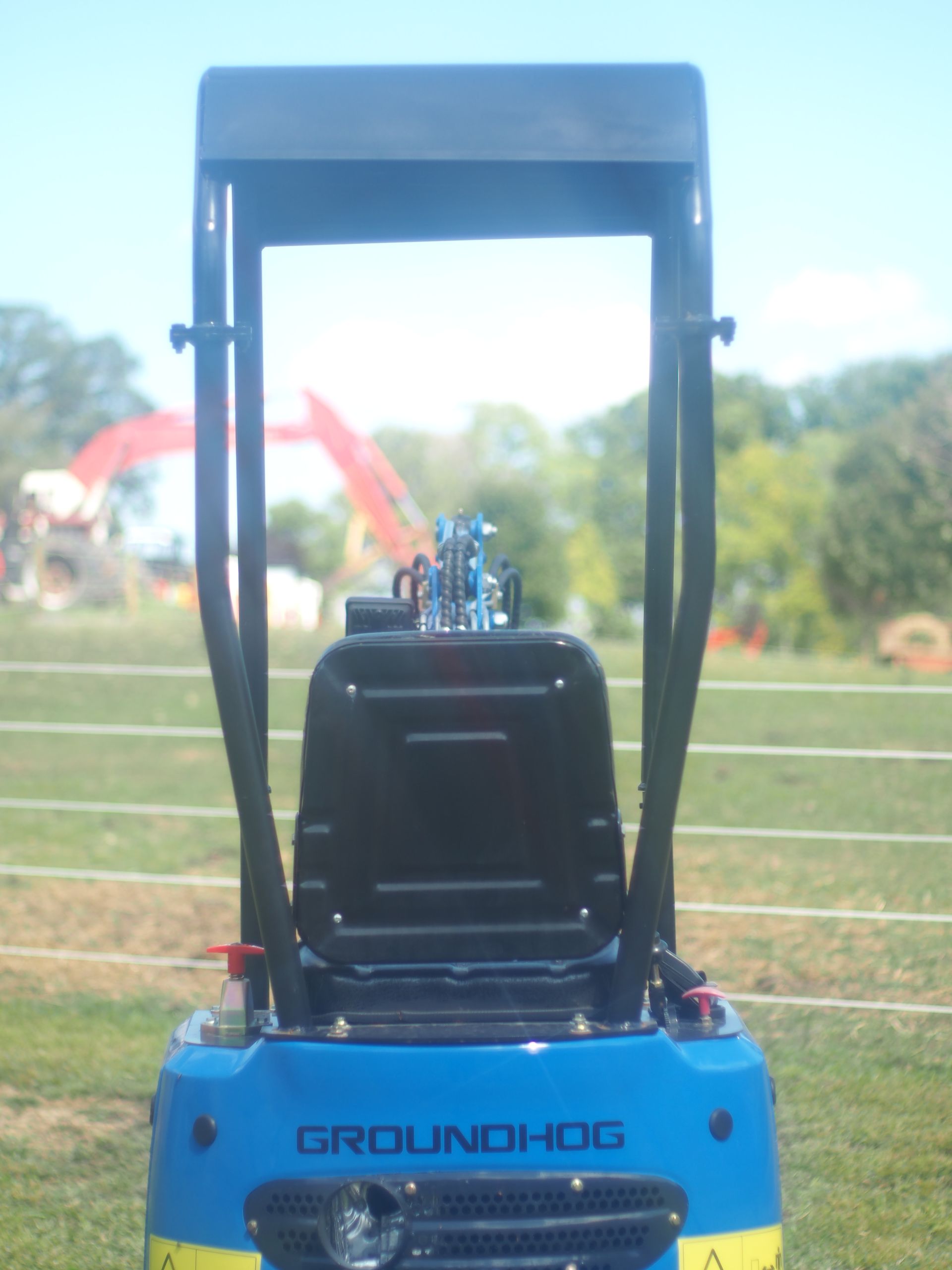 Blue and yellow Groundhog machine with a black seat and roll bar, outdoors.
