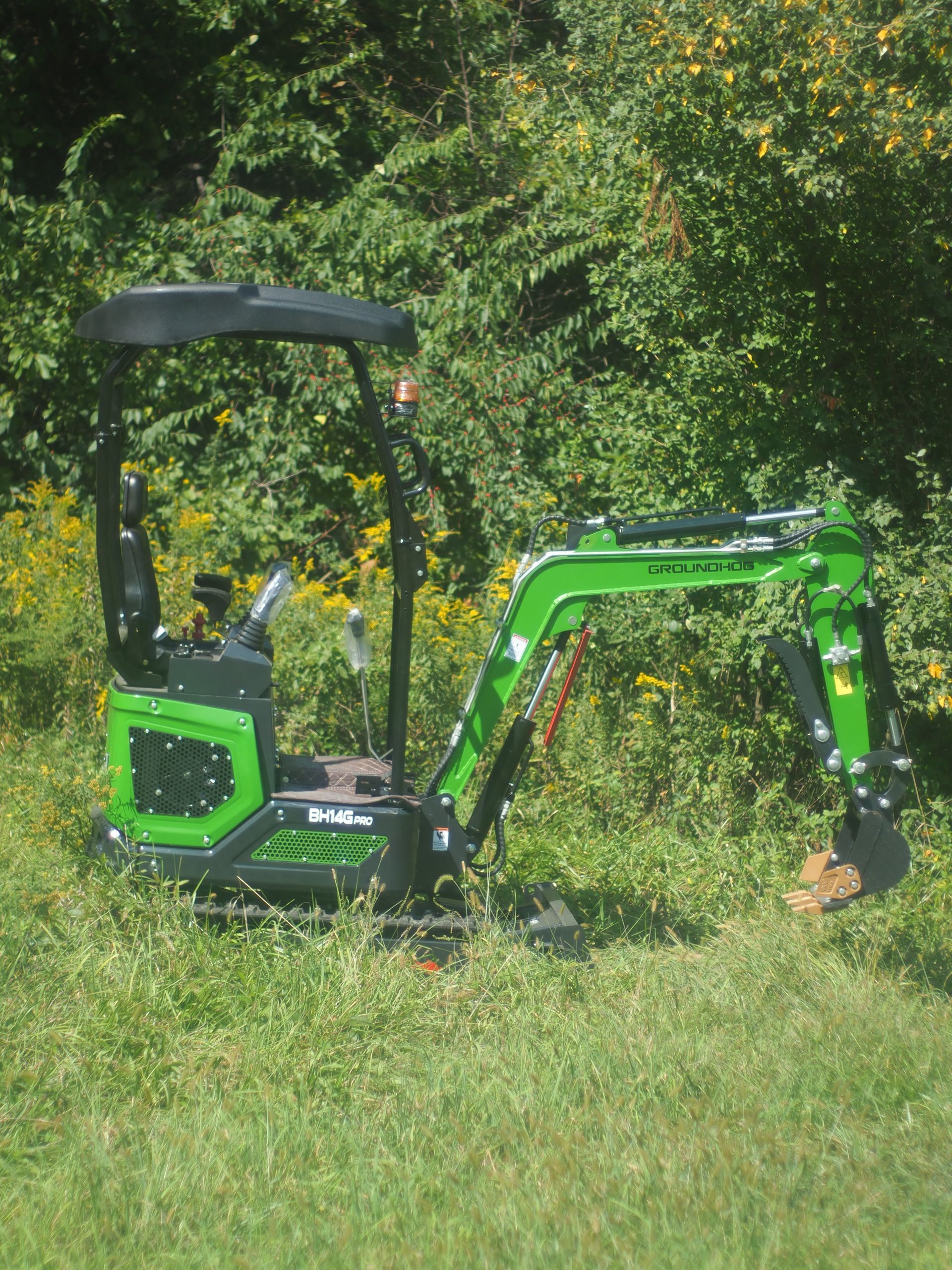 Green and black mini excavator in grassy area, arm extended.