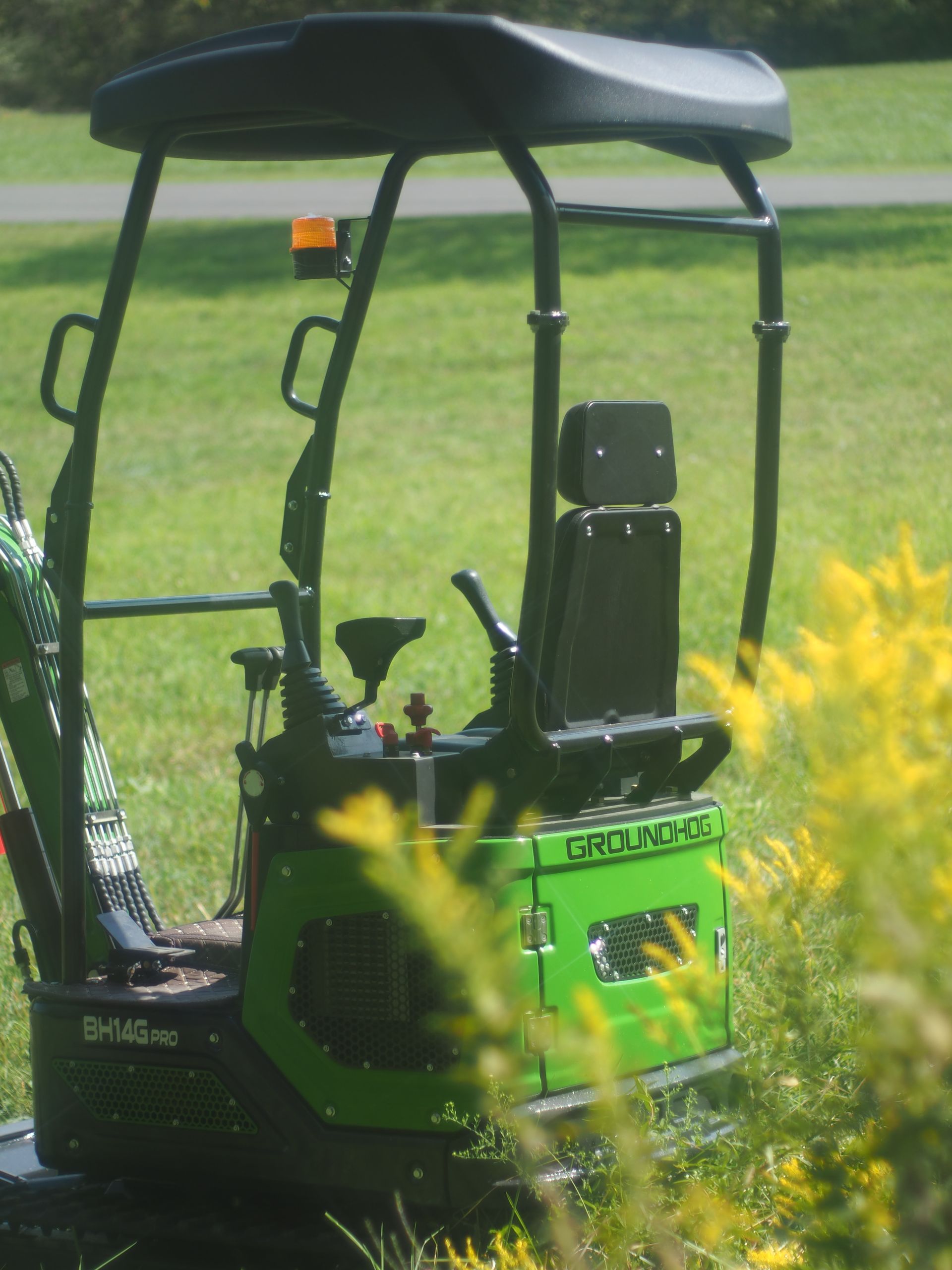 Green and black mini excavator with a canopy, sitting in a grassy field.