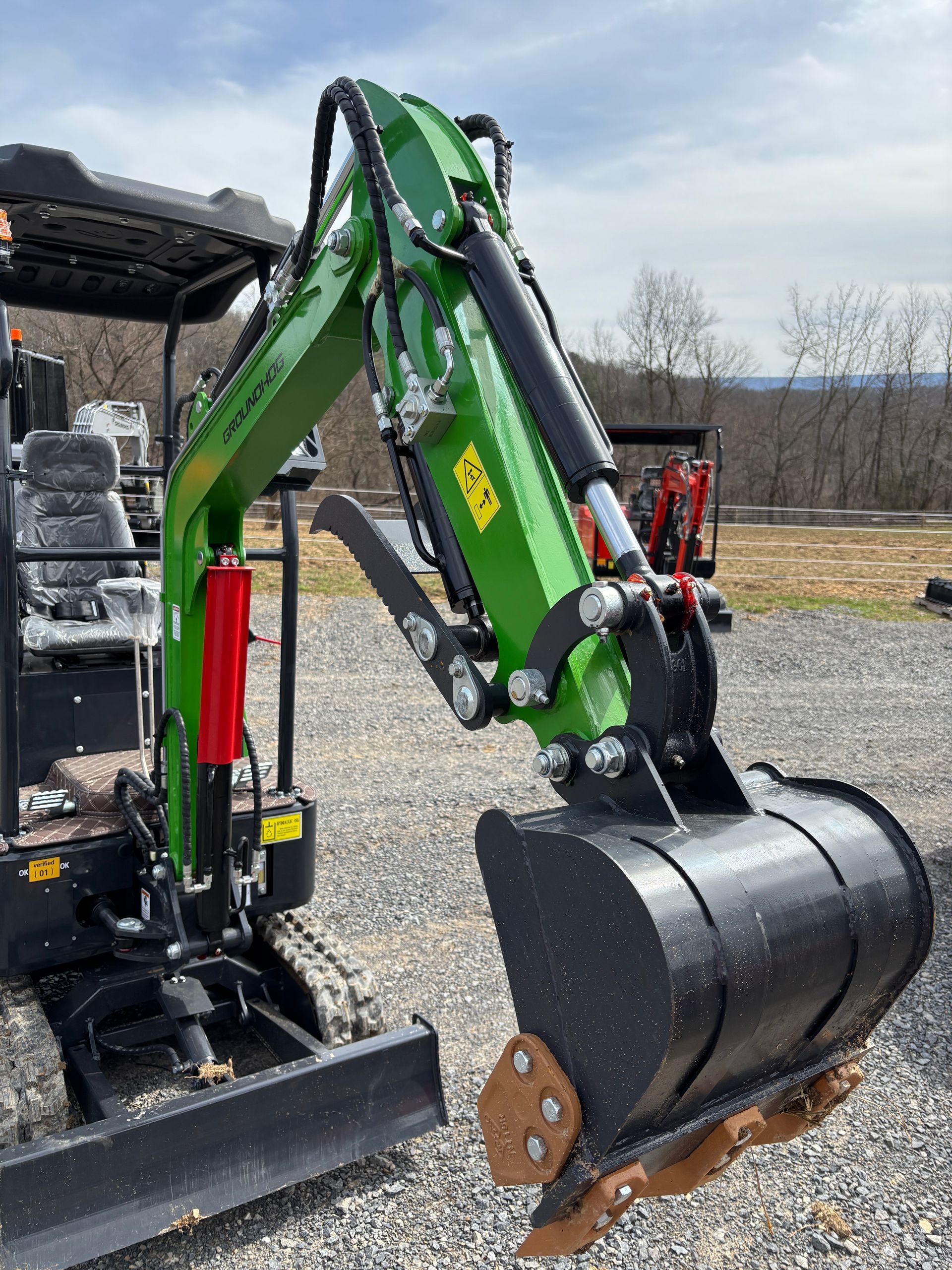 Green and black mini excavator, outdoors, angled view of the bucket and arm.