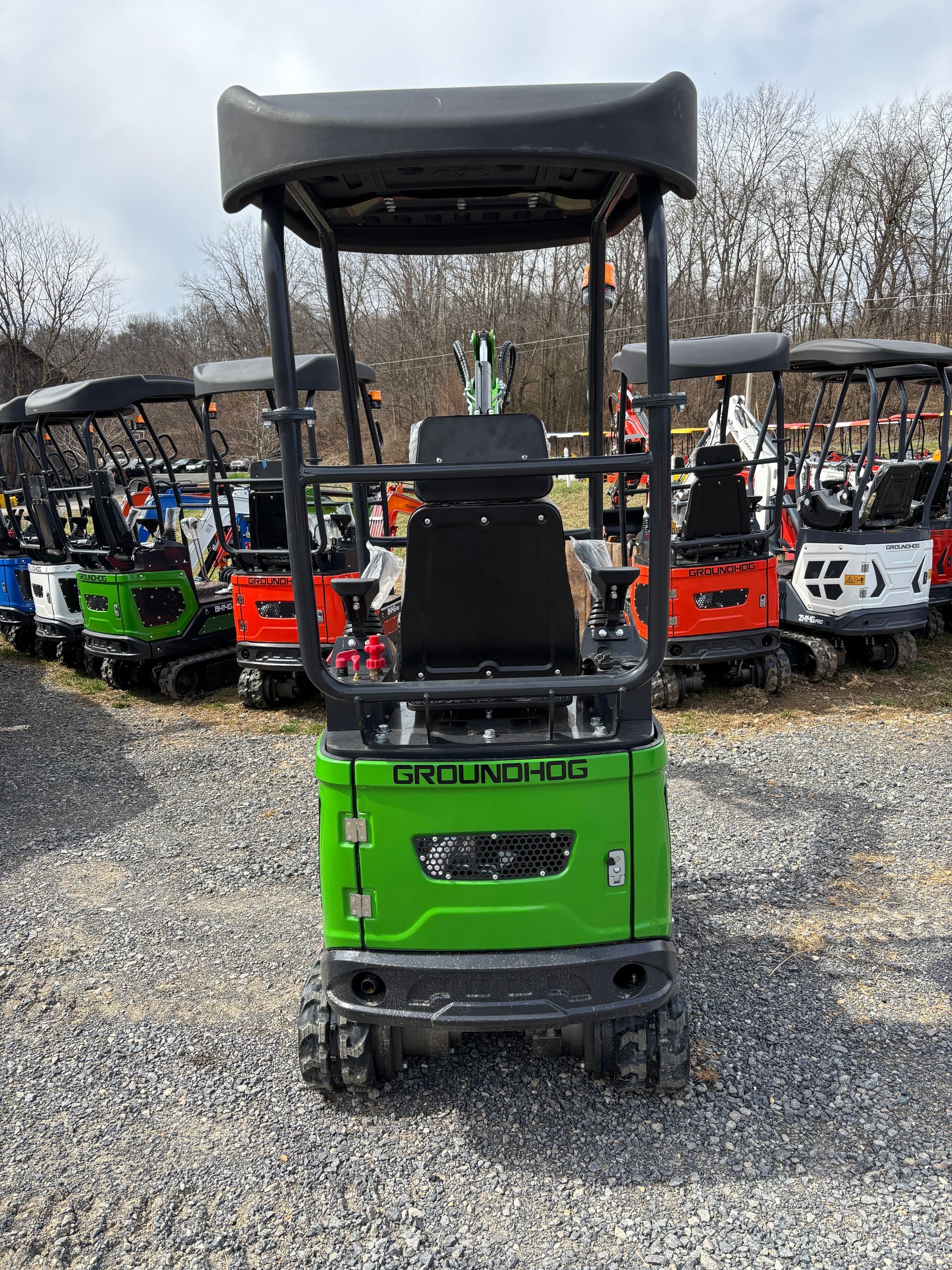 Green mini excavator with black canopy, parked outside with others.