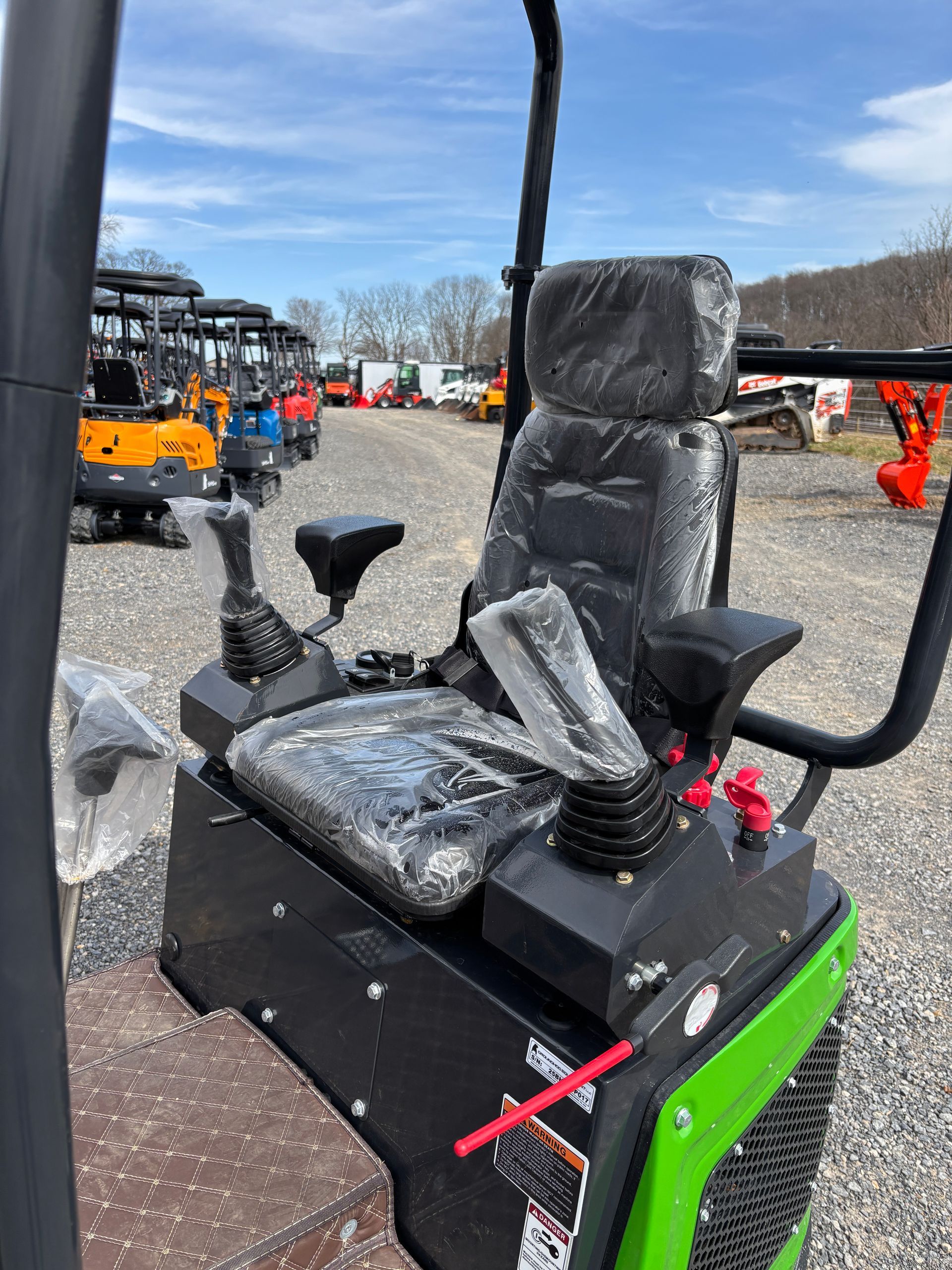 Black and green mini excavator cockpit with seat, levers, and controls, outdoor setting.
