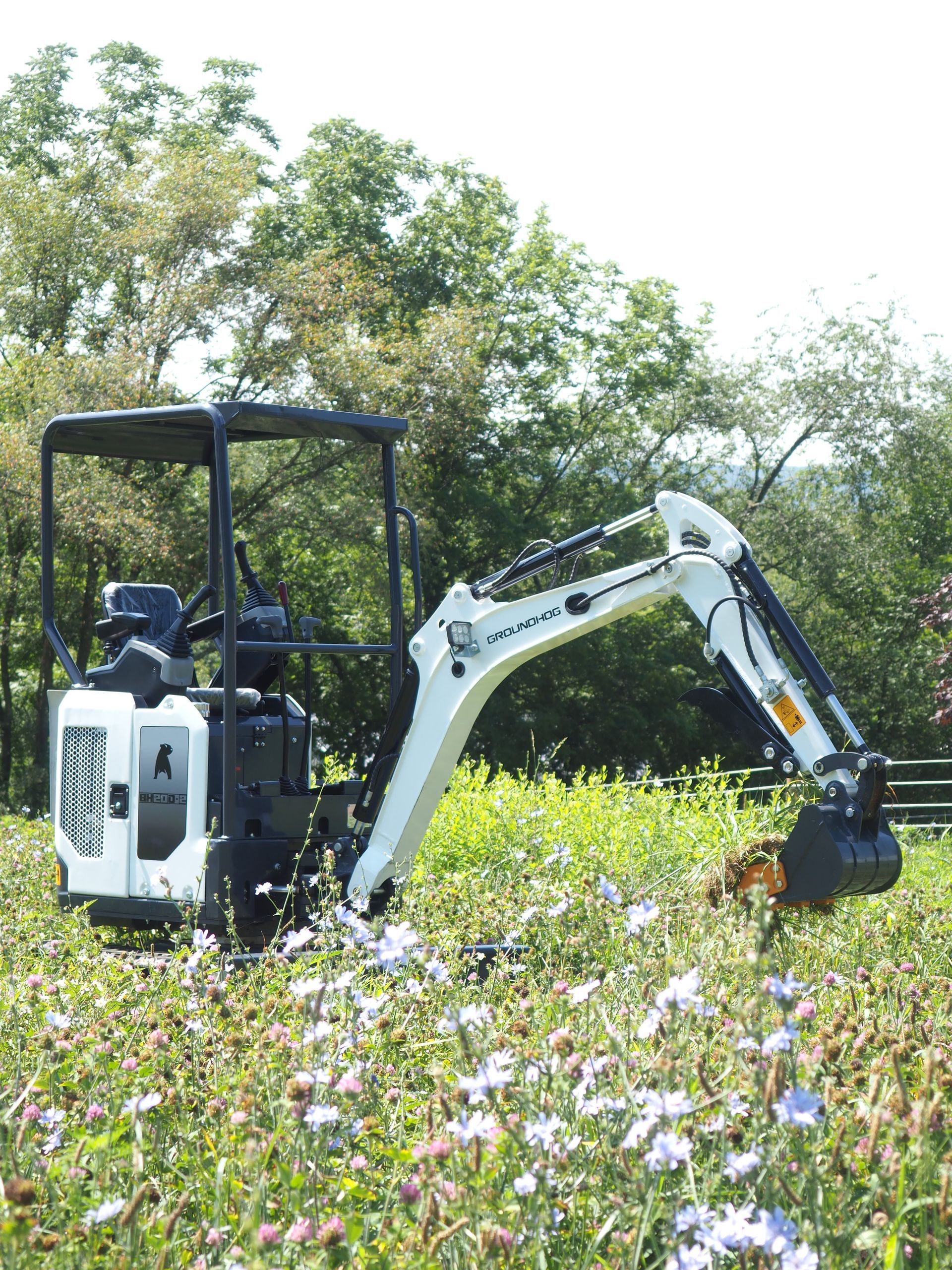 Mini excavator in white and black, digging in a field of wildflowers.