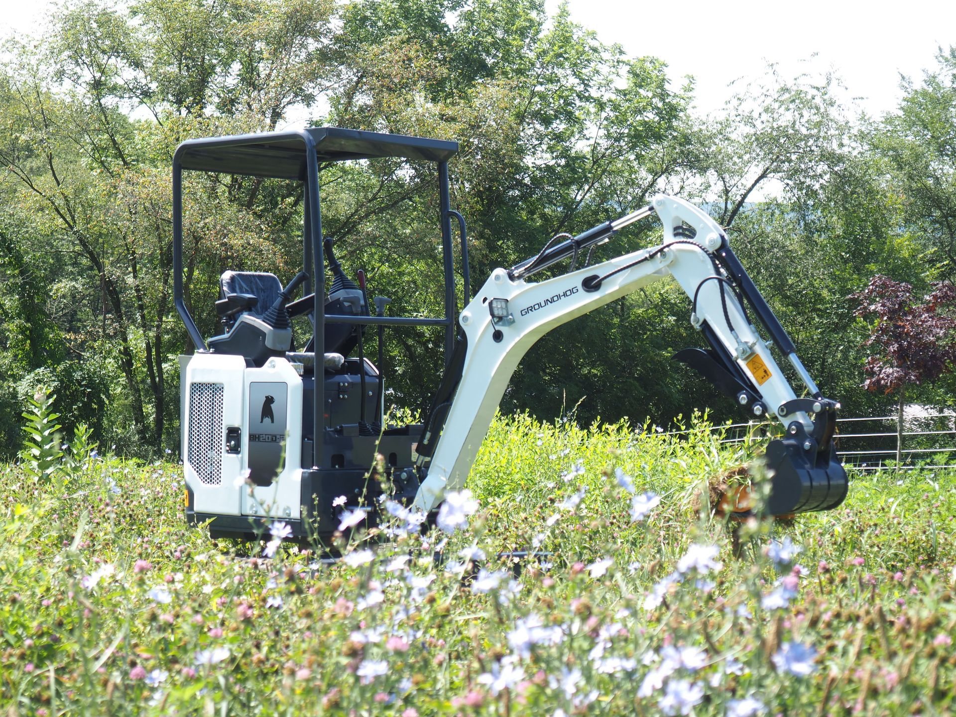 White mini excavator in a field of wildflowers.