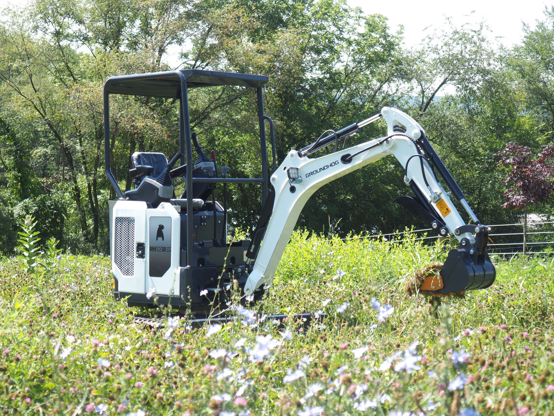 Small white excavator digging in a field of wildflowers.