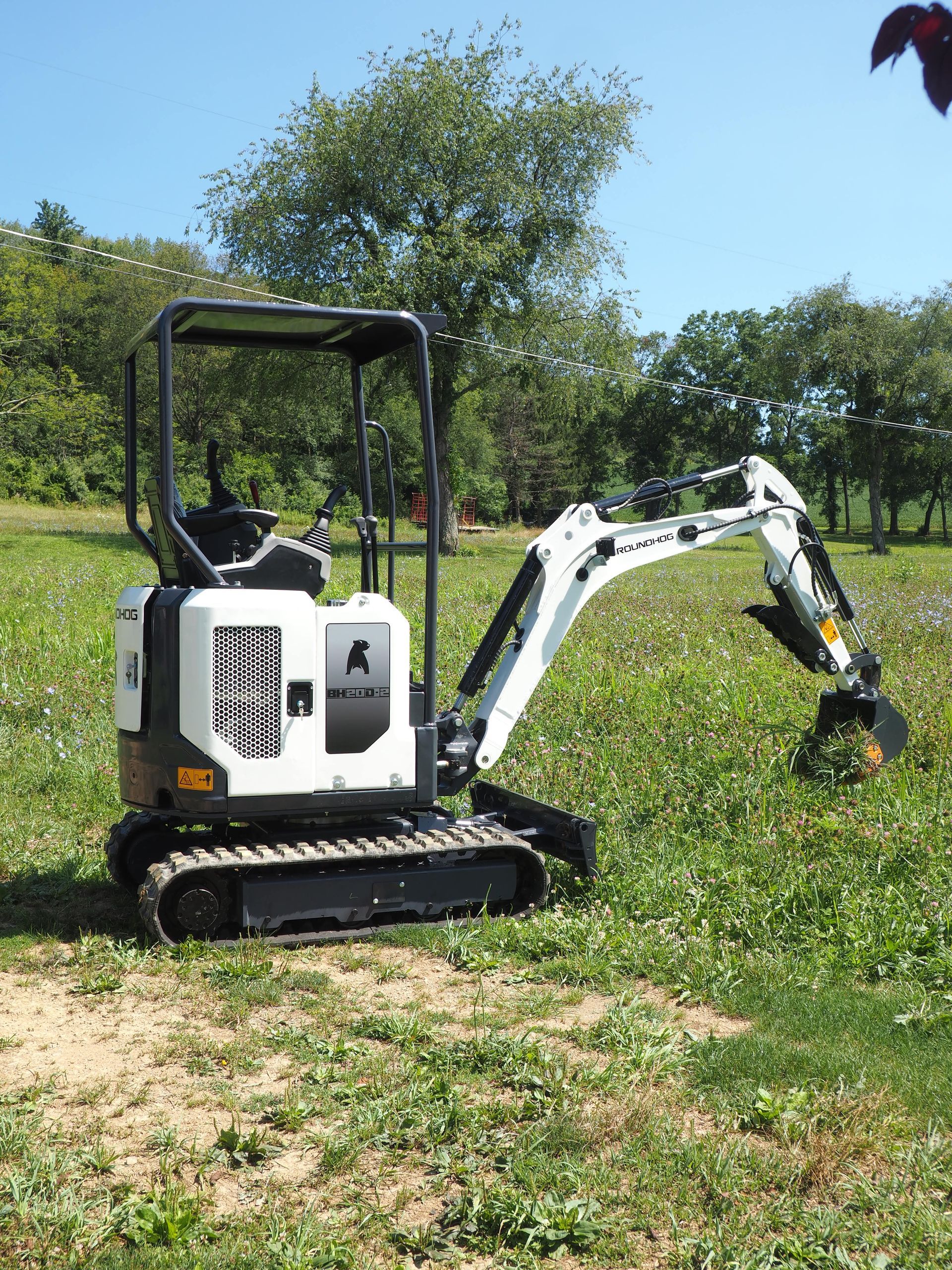 Small white Bobcat excavator on grass in a sunny field.
