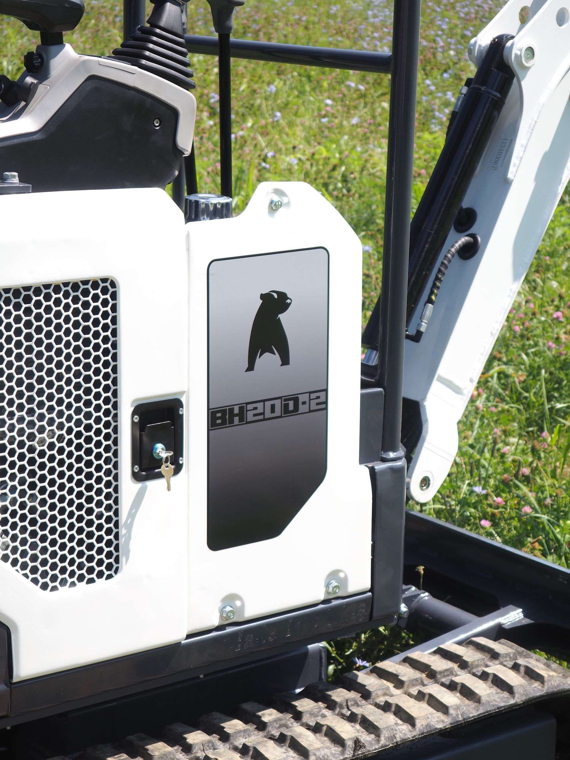 White mini-excavator with a black dog logo, black treads, and metal grating panel.