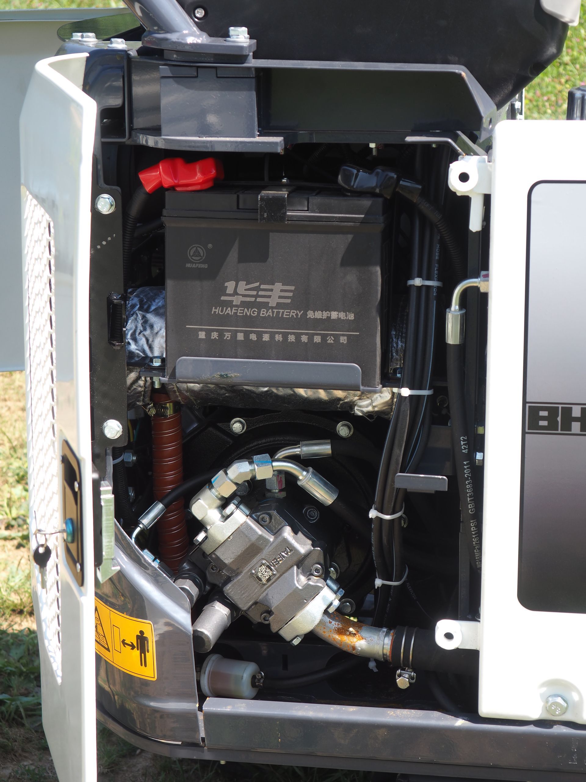 Open access panel of a machine, revealing battery, hoses, and engine components.