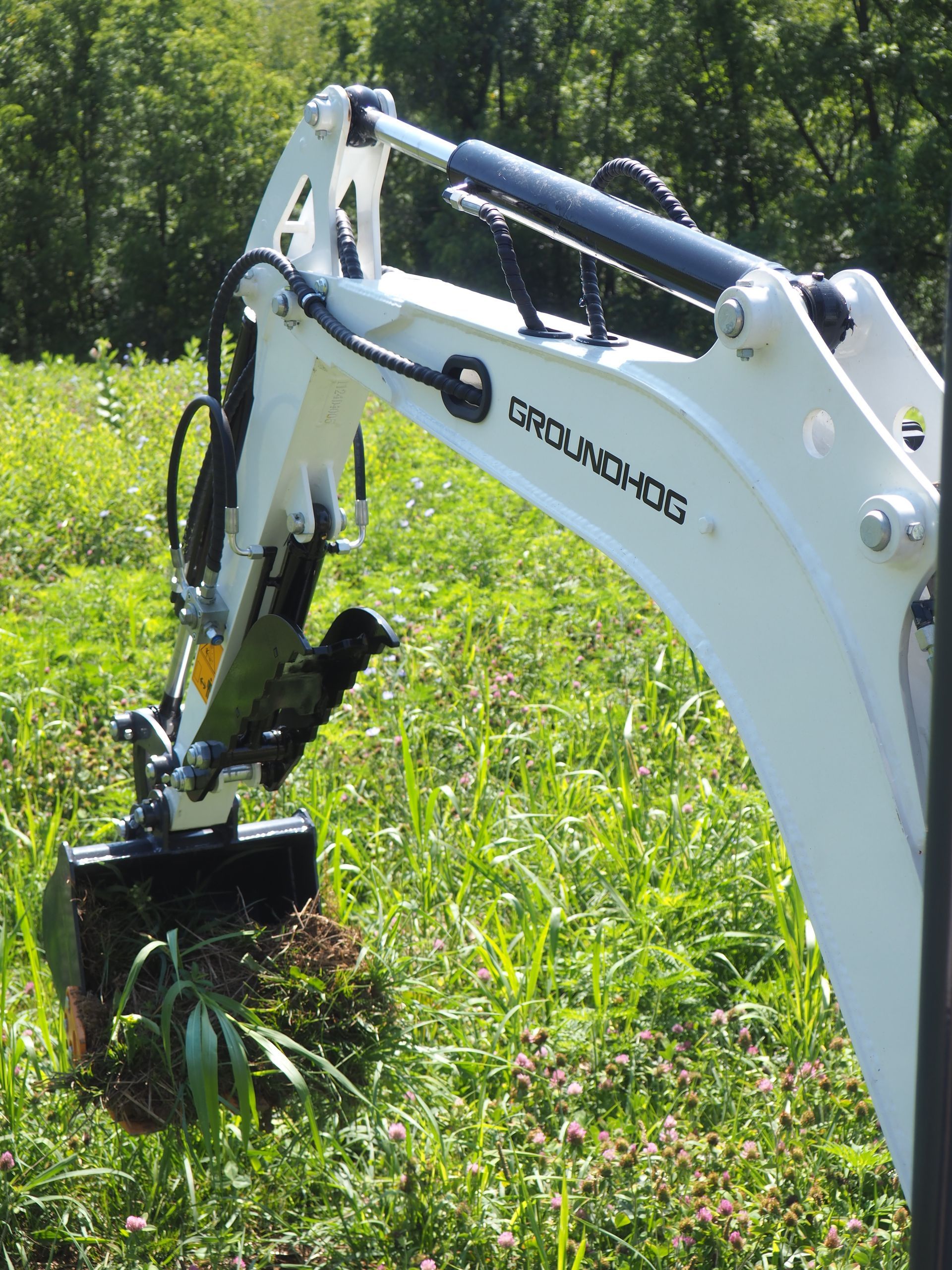 White Groundhog backhoe bucket digging in a grassy field.