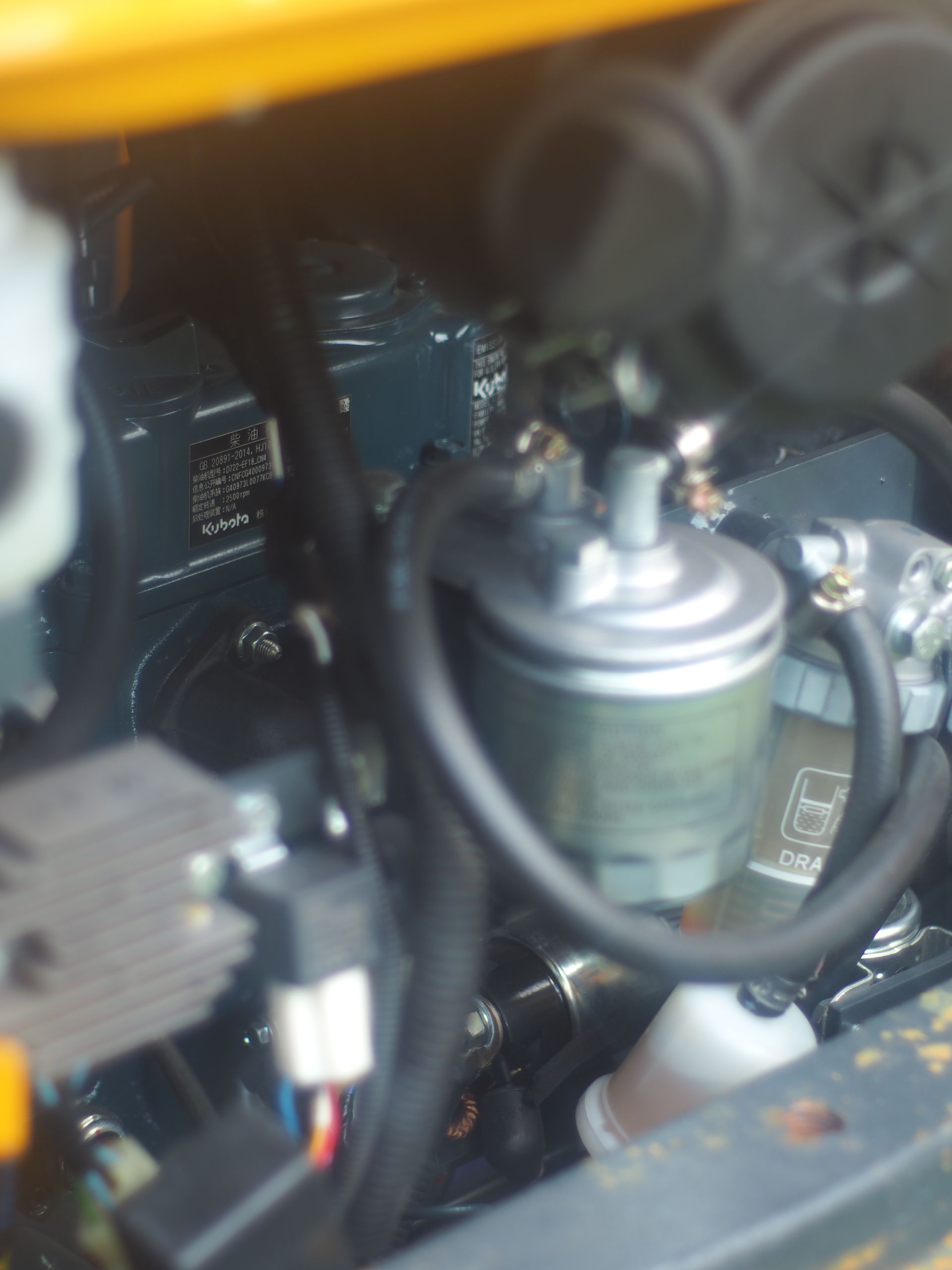 Close-up of a small engine with fuel filter and hoses; dark colors.
