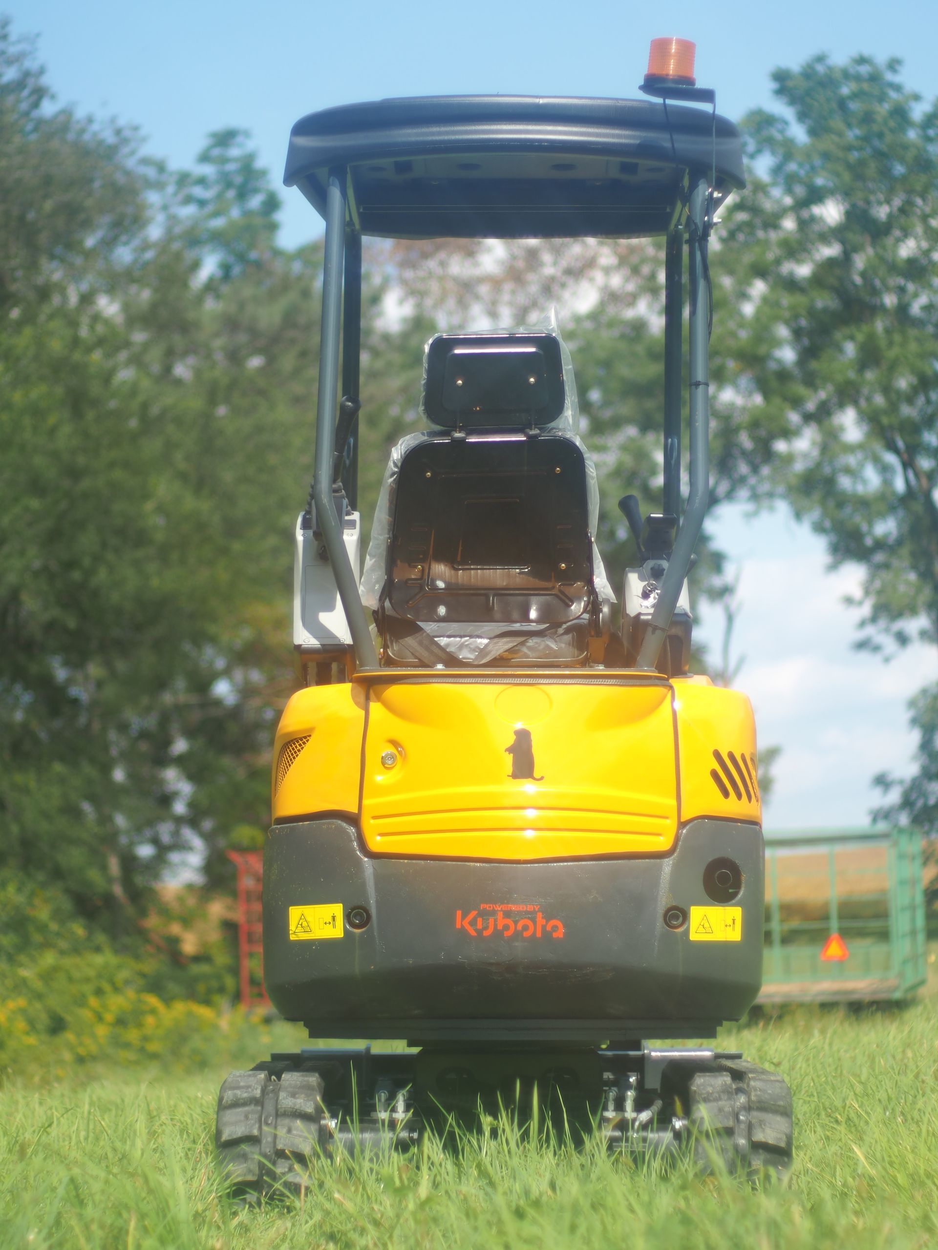 Yellow mini excavator on grass with black cab, safety light, and black seat, outdoors.
