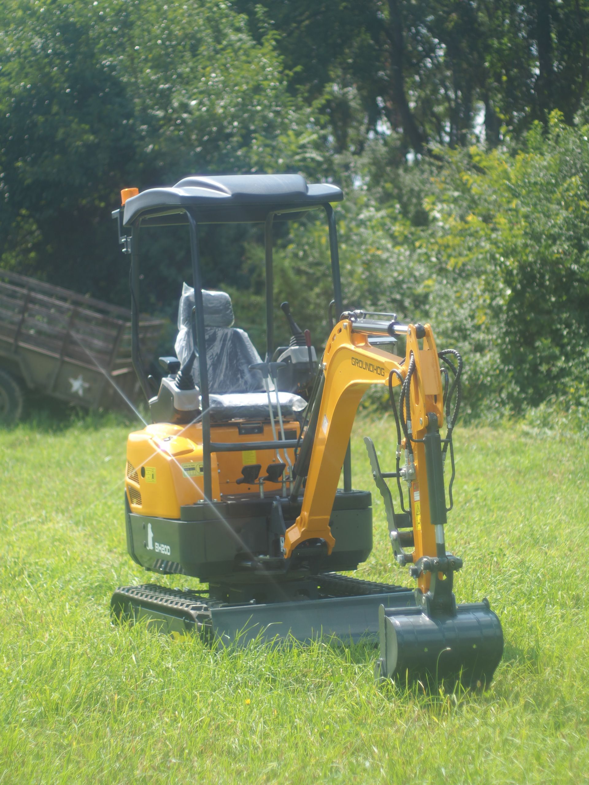 Yellow mini excavator on grass, near trees.