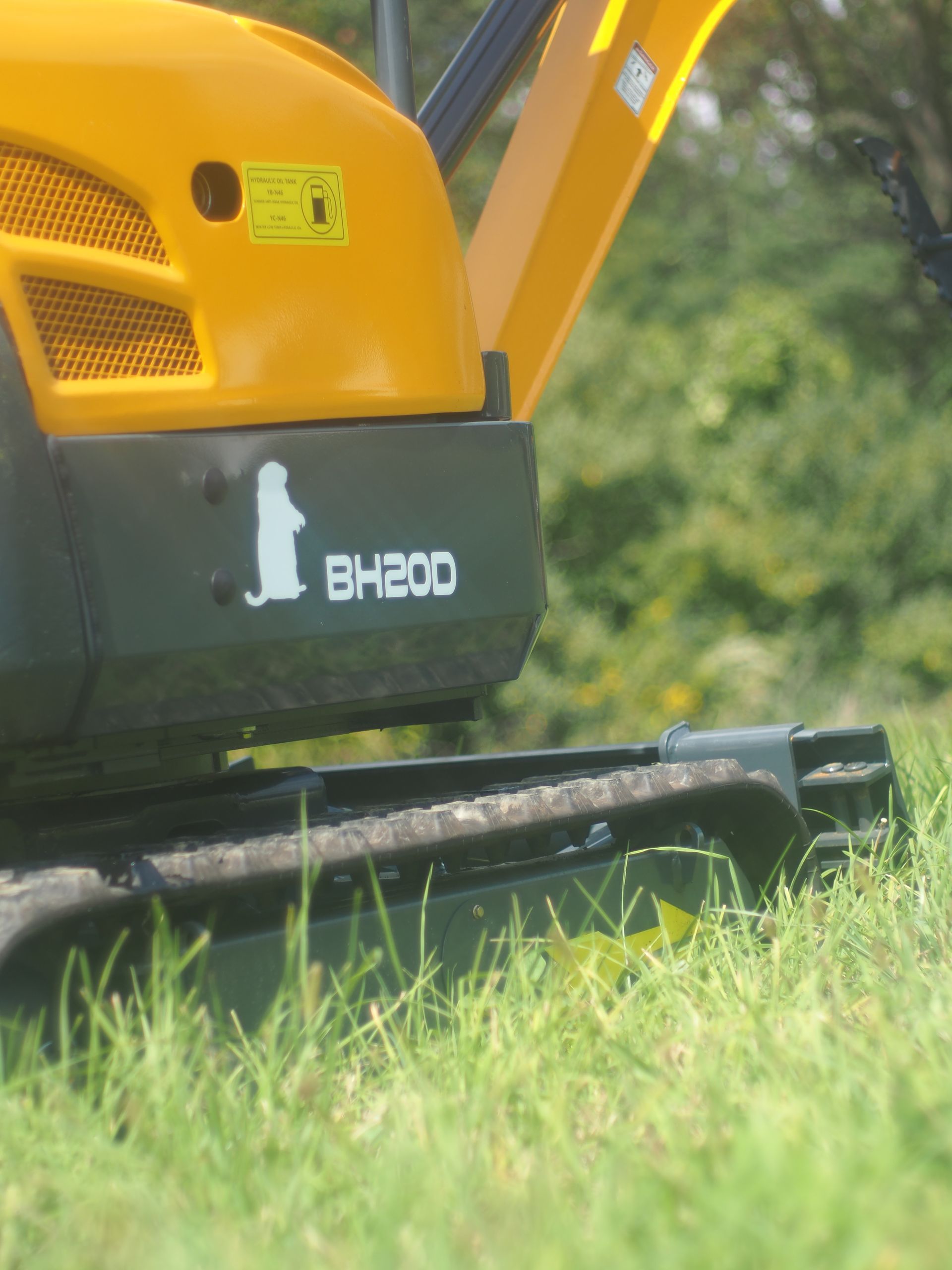 Yellow and black excavator detail with BH200 label and dog logo on grass.
