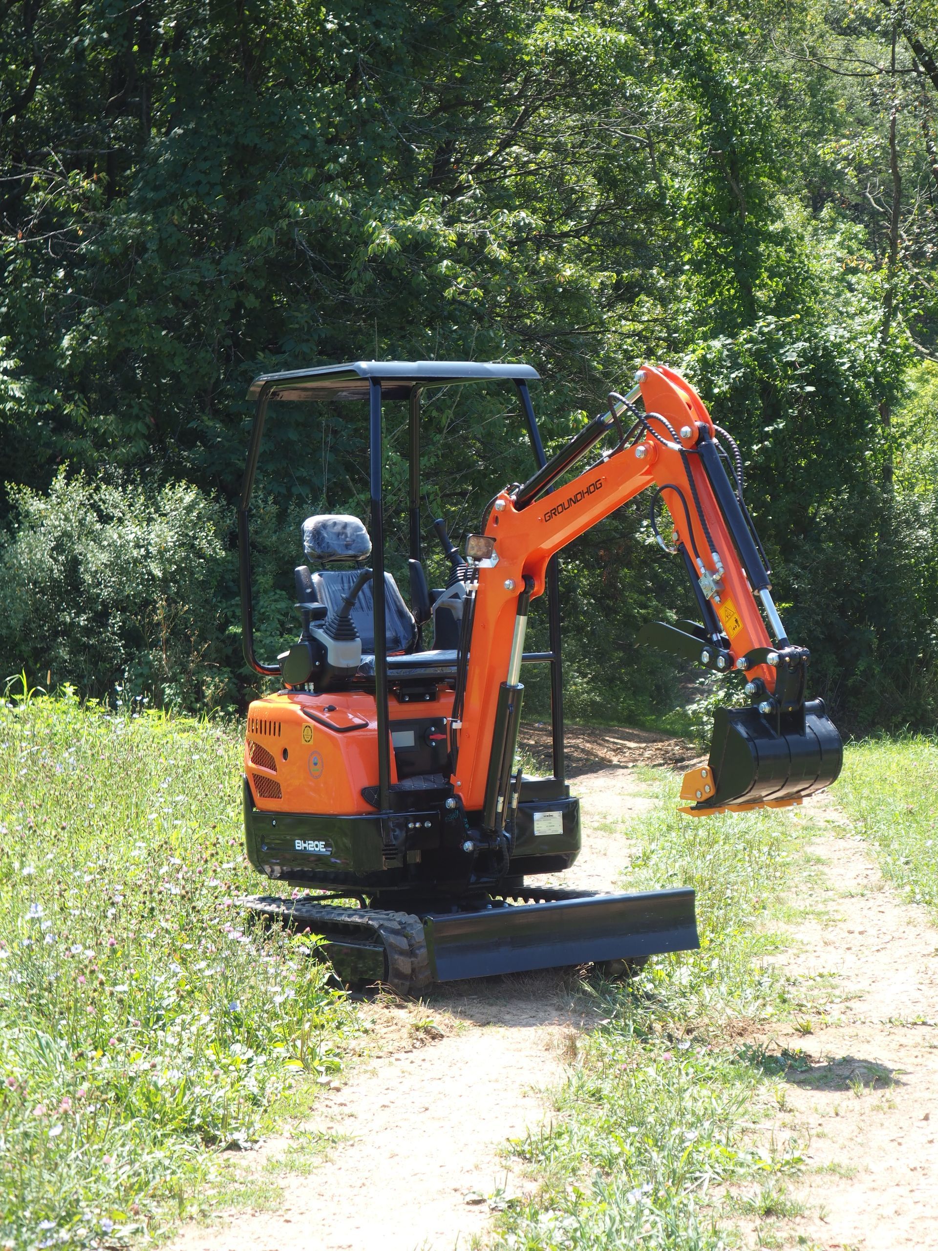 Orange and black mini-excavator on a dirt path in a wooded area.
