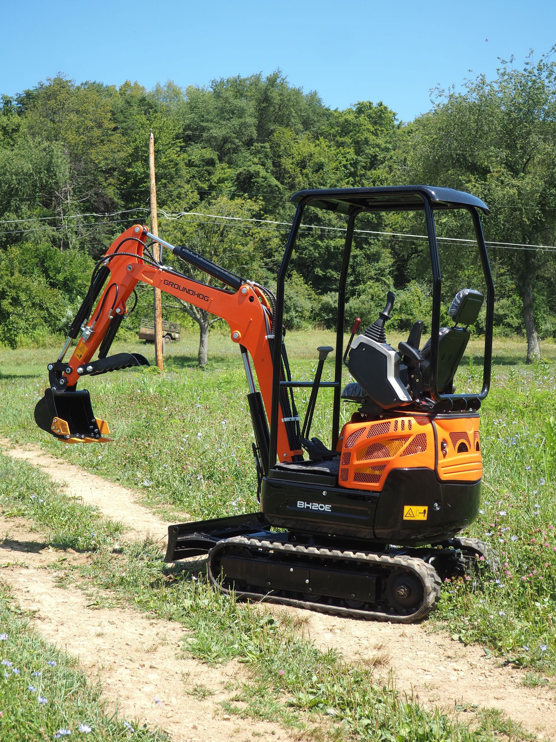Orange mini excavator on a dirt path in a field, with trees in the background.